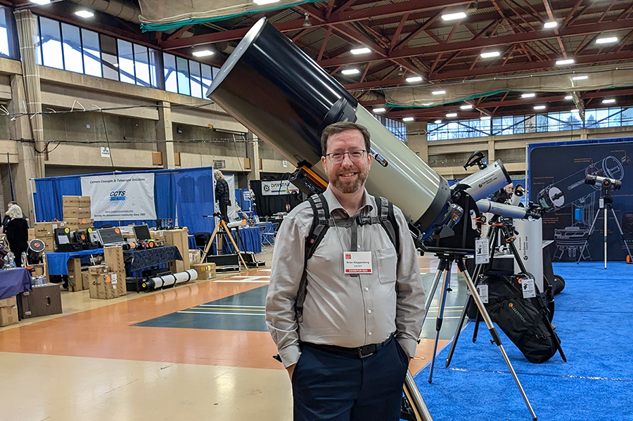 "Brian Kloppenborg stands in front of several telescope at NEAF"