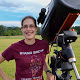 Smiling young woman standing in a field next to a telescope