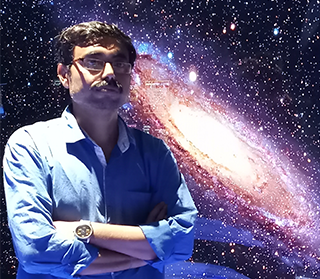 Man standing with arms crossed in front of an large astrophotograph of a galaxy